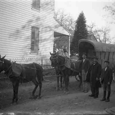 mules & covered wagon, 3 men/ 3 women & child on porch beside church