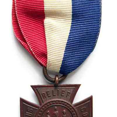 This image depicts the Women's Relief Corps badge associated with Mary Shellman, featuring a bronze cross-shaped medal with the inscription "Woman's Relief Corps 1863" and a central emblem showing three figures; it hangs from a red, white, and blue ribbon attached to an ornately designed clasp.