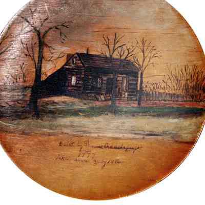 The wooden plate, painted by Mary Shellman, features a painted depiction of a log house with barren trees, inscribed with historical details about its construction by Thomas Addelsperger in 1777 and its demolition in 1886.