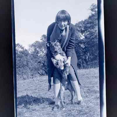 Negative of Emma Cohen Bray holding a dog upright (outside)