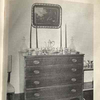 Photo of Hepplewhite Chest with caption: Wood chest with crystal dishes on top and decorative picture hanging on wall above the chest