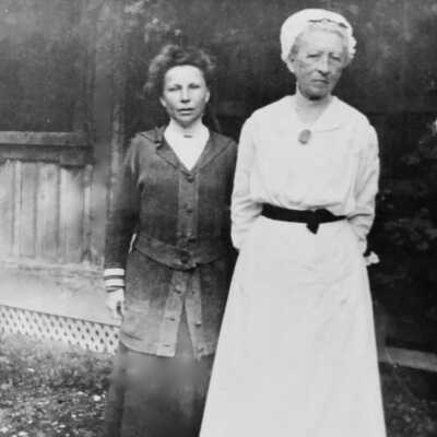 Emilie Gibbons Cohen + Miss Herbitt, her companion. taken at Fernside approx 1915: Two women standing in front of Summer house at Fernside. Emilie in the white and Miss Herbitt in dark.