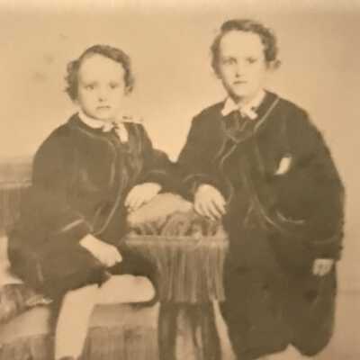 Augustus and Edward Bray: Twins are dressed in short pants, button boots sitting and leaning on arm of couch with fringe
