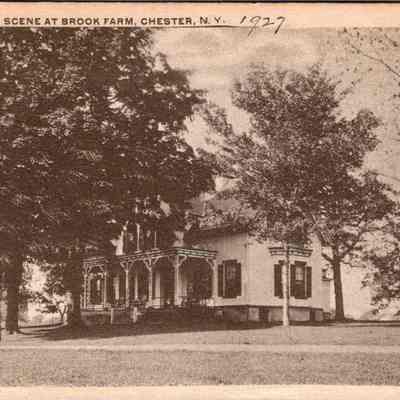 Residence and Scene at Brook Farm.Chester, N.Y. Front chs-019947-3: The image displays a vintage photograph of the residence and scene at Brook Farm, located in Chester, New York, dated 1927. The photograph features a large, elegant two-story house, characterized by its prominent architectural details including a covered porch with ornamental railings and a series of rounded archways. The house is partially obscured by lush, mature trees which add to the serene, pastoral ambiance of the setting. Above the treetops, a clear sky appears, suggesting a calm, bright day. The foreground of the picture is dominated by a well-maintained lawn, enhancing the stately presence of the home in its tranquil, rural environment. The aged quality of the photograph contributes to the historical charm and allure of the scene, capturing a moment in time in the early 20th century American landscape.