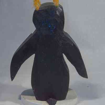 Rockhopper Penquin - back: A carved wooden penguin sculpture features two yellow feather-like protrusions atop its head.