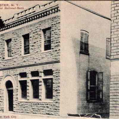 “Chester, N. Y. Chester National-Bank” Front chs-019952-2: The image portrays the Chester National Bank located in Chester, New York, featuring an early 20th century architectural design. The building is constructed from textured stone blocks with distinctively shaped windows and an entrance framed by an ornate arch. Adjacent structures include a two-story building to the left with signage indicating a business perhaps selling Pilsner beer, and another brick structure to the right. The scene, captured in black and white, suggests a quiet street corner in a small town, and the photograph bears the mark "Artino post-cards New York City," indicating its origins as a postcard from the era.