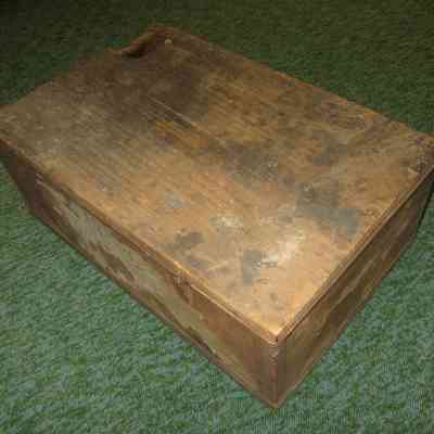 Wooden Box with obscured writing on lid: A weathered, rectangular wooden crate rests on a green carpet.