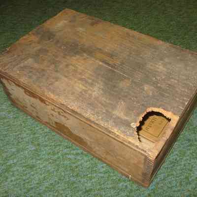 Wooden Box with obscured writing on lid: A worn wooden box on a green surface has a hole int he lid.