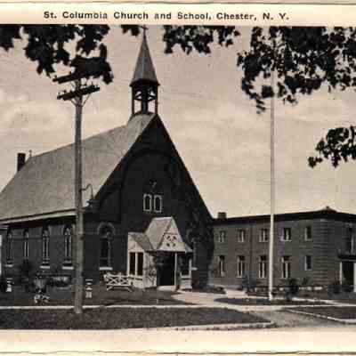 20826 St. Columba Church & School.: The image depicts the 1887 St. Columbia Church and the School built in 1908 located on High Street, Chester, New York, showcasing an expansive view of both Gothic-style church architecture with a steep arch and a pointed bell tower, and an adjacent three-story school building featuring a classical facade with columns. The scene is further enhanced by verdant lawns, leafy trees, and a clear sky, captured in a serene, black-and-white photograph, evoking a sense of historical significance and community importance during the early 20th century.