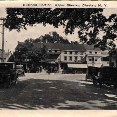 20827 Business section, upper Chester.: This vintage photograph depicts Durland Square, the business section of Upper Chester, N.Y., featuring early 20th-century automobiles, and a round horse watering trough in the middle of the intersection of Main St and Academy Ave.
