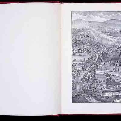This image shows a detailed two-page spread from a book. On the left side, there is text under the heading "GREENWOOD IRON WORKS of P. P. PARROTT, 1875," describing the history and significance of the Greenwood Iron Works located in the Ramapo Mountains, detailing its role in iron ore smelting and operation during the Revolutionary War and beyond. The right side features a detailed illustration depicting a panoramic view of the Greenwood Iron Works with numerous buildings, a tower, smokestacks emitting smoke, a train running along tracks, and the surrounding hilly landscape densely covered with trees. This descriptive and visual documentation captures both the industrial and natural aspects of the area historically.