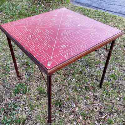 Chester Grange Card Table: A red and brown wooden card table with printed advertisements for local businesses stands on grassy ground outside.