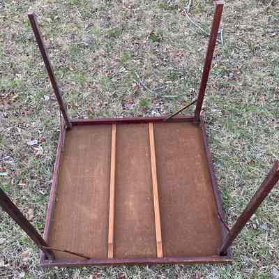 Chester Grange Card Table underside: An overturned wooden card table with detached legs lies on the grass and scattered leaves outdoors.