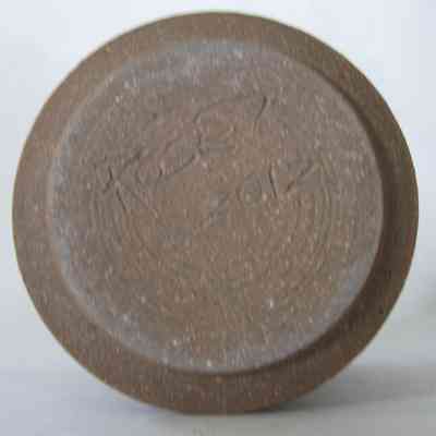 Brown Nativity - bottom: The image shows the underside of a textured, clay pottery piece with engraved markings.