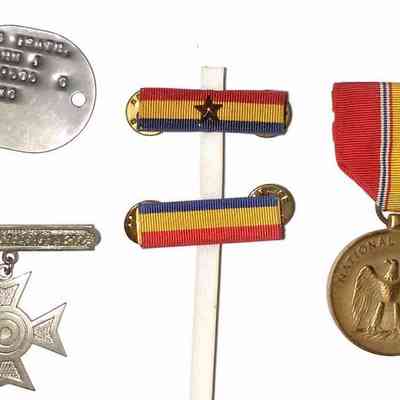 John J. McGrath's Korean War Service Medals - recto: The image displays John J. McGrath's Korean War military memorabilia, including various medals and badges of different sizes, shapes, and colors. Among them, there are two circular medals with ribbons, both inscribed with "U.S. Marine Corps," showcasing different ribbon patterns; a metal tag with inscribed text, typically used for identification; a small oval medallion with an embossed figure; a cross-shaped badge; and two ribbon bars in red, yellow, and blue, with one featuring a central star.