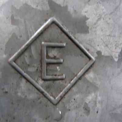 chs-014026 Erie RR Tall Spout Oil Can left side - Erie Logo.jpg: The image shows a close-up of the left side of the  Erie RR Tall Spout Oil Can with an embossed letter "E" inside a diamond-shaped border - the Erie RR logo.