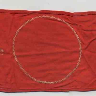 Chester Inn souvenir: German WWII Political NSDAP Armband reverse.: The image shows a red fabric with a stitched circle, featuring faded white text and a label.