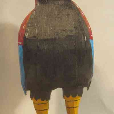 Rooster - front: The image shows a colorful, painted wooden rooster sculpture with vibrant red, blue, and yellow patterns.