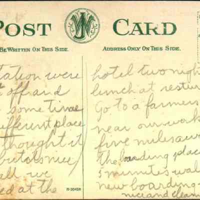 Address side of the "Erie Depot, Goshen, N. Y." postcard.: The image shows an antique postcard featuring handwritten messages. There's a green print of "POST CARD" at the top and a circular logo with a "WJ" monogram in the center. The right side of the card, meant for addresses, includes postal rate information and a placeholder for a stamp. The handwritten text recounts personal experiences, mentioning a stay at a hotel, having lunch at a restaurant, and visiting a farmer's place nearby.