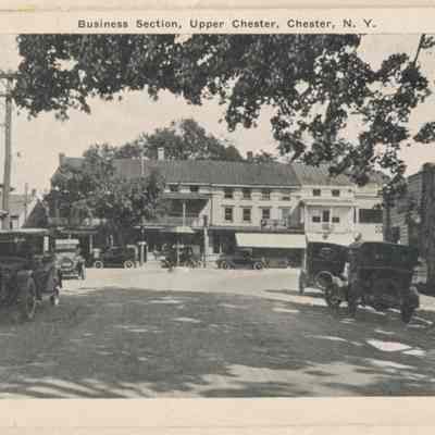 Business section, upper Chester.: The image depicts the business section of Upper Chester, NY, showcasing early twentieth-century cars and architecture.