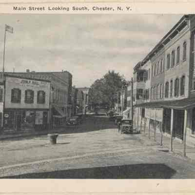 Main Street looking south.: This vintage black-and-white postcard depicts Main Street in Chester, New York, showcasing old buildings and