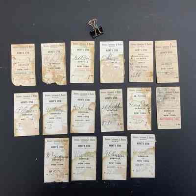 The image displays a collection of 16 vintage "Delaware, Lackawanna & Western Railroad" agent's stubs, arranged neatly in three rows against a dark background. Each ticket features handwritten details, indicating trips between Denville and New York, with various dates from the early 1900s such as September 1900, October 1904, and August 1904. The tickets show signs of aging, with visible creases, discoloration, and worn edges, suggesting frequent use. Above the tickets, there is a small metal binder clip, possibly used to keep them together. The overall arrangement presents an appealing historical snapshot of early 20th-century rail travel documentation.