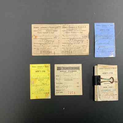 The image displays the front of a collection of vintage train tickets from the Delaware, Lackawanna & Western Railroad, each with distinct colors, handwriting, and dates. Two beige tickets on top left are labeled “Mileage Exchange Ticket,” issued in 1892, while a blue ticket dated for 1904 sits on the top right. Below, a yellow agent’s stub ticket from 1904 and a beige half-ticket from 1900 are visible. On the right, a stack of tickets bound together includes one for December 1905. The tickets showcase various details like destinations, passenger information, and validation markings, offering a glimpse into early 20th-century rail travel.