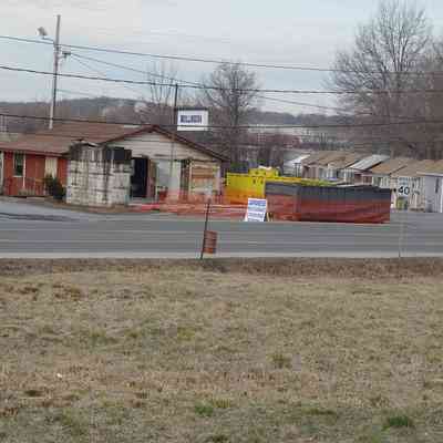 Dillinger's demolition with neighboring rental cabins visible.: An old building and construction site are seen beside a road with orange fencing around it.