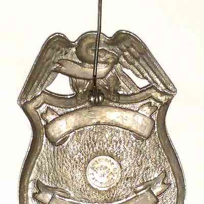 Erie Railroad Watchman Badge - back, pin open.: The image shows a metallic pin-back badge with eagle design, featuring text and circular markings.