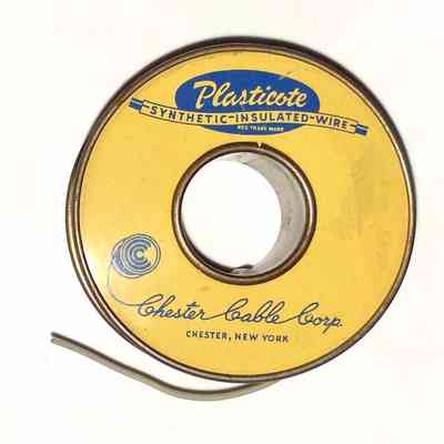 Insulated Wire Spool. Chester Cable Corp. - Side B: The image displays a circular spool labeled "Plasticote Synthetic-Insulated-Wire" in blue text atop a yellow background, with "Chester Cable Corp." written in script, indicating it originates from Chester, New York; the spool is partially used, revealing some of the gray wire coiled around it, while the colors and design reflect a classic or vintage appearance, the product is from mid-20th century.