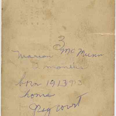 Address side of the "Marion McMunn baby photo postcard": The address side of th this postcard shows an aged, stained piece postcard displaying handwritten text, including the name "Marion McMunn",born 1913", and some notes indicating "3 months" and "home Graycourt". The paper has rough edges and is soiled.