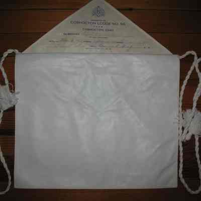 Apron: Printed on paper on the reverse side of flap: "Presented by Coshocton Lodge No. 96 F&AM, Coshocton, Ohio to Brother A. VanDer Weele". Dates of initiation: E.A. Juen 11, 1970, F.C. Sept 24, 1970, M.M. Oct 20, 1970. White imitatiob leather candidates apron, lined, cotton cord and tassels