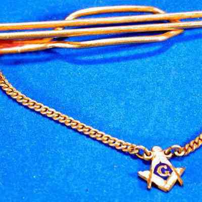 Clip: Tie clip with Square and Compasses suspended on chain. Gold color