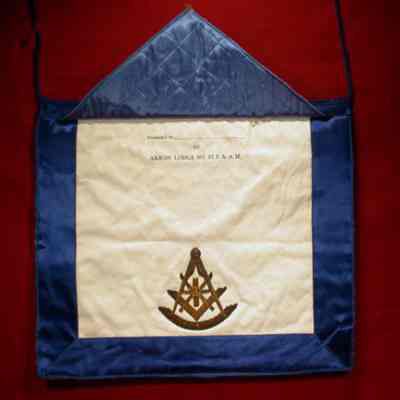 Apron: Past Master, white leather with blue edging, blue satin backing. Past Master's emblem stitched in gold on face. "Presented by Akron Lodge #83" under fla. 12 1/2" x 14 3/4"