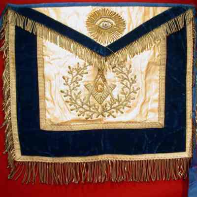 Apron: White satin with blue felt edging and silver tassels. All Seeing Eye on fla and Square & Compasses on body all stitched in gold and silver, white cotton backing. 13 1/2" x 15 1/2". LIXX Orete? $13.00 under flap