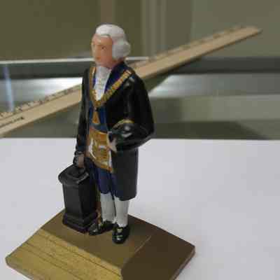 Figurine: Plastic figurine of George Washington standing by Master's pedestal wearing the Grand Master's Jewel and Masonic apron. From Chicago by F.N.K. Co.