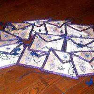 Aprons: Set of 12 officers aprons from New England Lodge #4 (WM, SW, JW, SD, JD, SS, JS, Secy., Treas, Chap, Tyler, Musician). White satin with blue trim and designs.