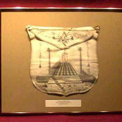 Apron: White lambskin apron with top flap torn off. Sanctum Sanctorum on body square and level on flap. 12 3/4" x 14". Manufactured by "Valdenuiet" of New York City, 1797.