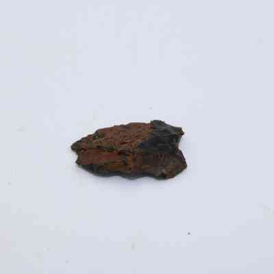 Closeup of small basaltic glass cortex flake: The image shows a basaltic glass cortex flake, displaying rough edges and a dark, glossy surface against a plain white background.