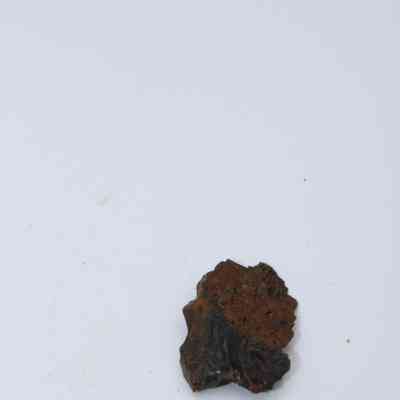 Closeup of basaltic glass cortex flake: A basaltic glass cortex flake, displaying its rough texture, lies against a plain white background, highlighting its brownish-black coloration and irregular shape.