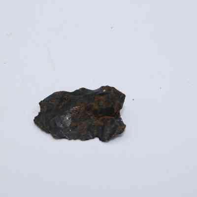 Closeup of basaltic glass cortex flake: The image shows a small basaltic glass cortex flake with a rough, dark surface and reddish-brown patches, lying against a plain white background.