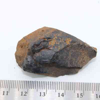 Closeup of basaltic glass core with metal ruler: A basaltic glass core is placed on a white surface alongside a measuring ruler for scale.