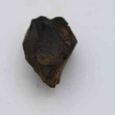 Closeup of lengthwise view of basaltic glass core: The image shows a rough, dark basaltic glass core with a slightly glossy surface and irregular edges, set against a plain background.