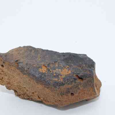 Closeup profile of basaltic glass core: The image depicts a basaltic glass core, characterized by its dark, glossy surface with natural irregularities, lying on a plain white background.