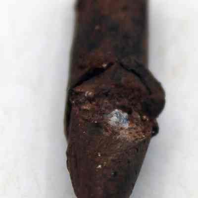 Lengthwise view of metal bullet: The image shows a small, brown, rusted bullet with a pointed end, lying on a light background, featuring rough texture and irregular surface marks.