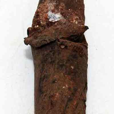  Lengthwise view of bullet: The image shows a rusted, cylindrical object resembling an old metal projectile, with a pointed tip and visible corrosion, lying on a white surface.