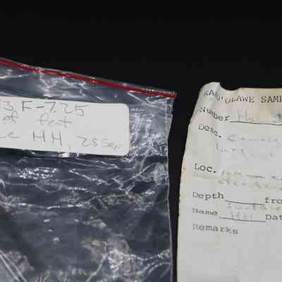 Artifact bag and slip for cowrie shell lure: The image shows a plastic artifact bag with a handwritten label beside a weathered, handwritten sample form detailing specifications and location.