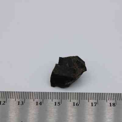 Basaltic glass core with ruler: The image shows a small, dark basaltic glass core placed next to a ruler for scale on a plain background.