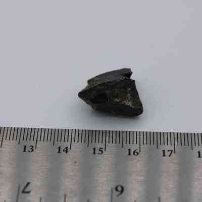 Closeup of small basaltic glass core above ruler: A small basaltic glass core is placed next to a ruler, providing a size reference against a plain white background.