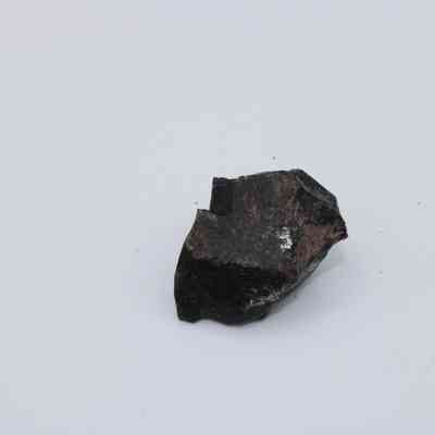 Closeup of basaltic glass core: The image shows a piece of basaltic glass core with a dark, shiny surface displayed on a plain white background, highlighting its natural texture.